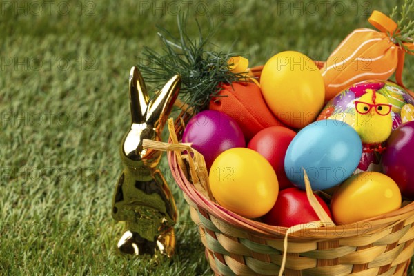 Colourful Easter eggs and a golden rabbit figure next to a basket on grass