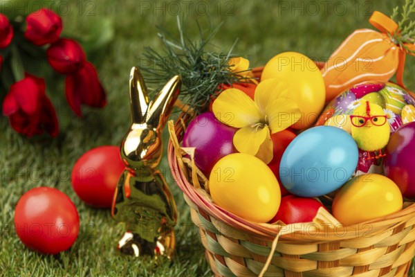 A basket with colorful Easter eggs and a rabbit statue on grass