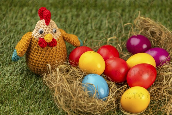 Crocheted chicken and colorful easter eggs in a nest on grass