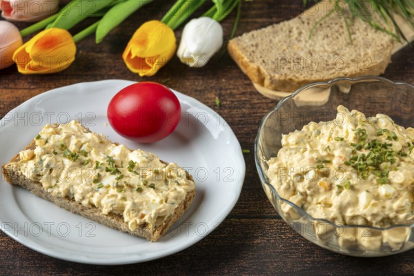 Egg salad on a plate with bread, surrounded by fresh ingredients and flowers
