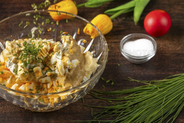 Chives fall into a bowl with ingredients for egg salad on wooden table