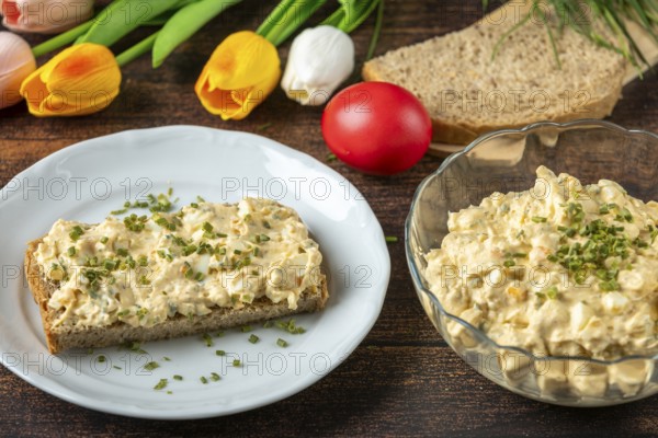 Slice of bread with egg salad on plate, with fresh herbs, tulips in the background