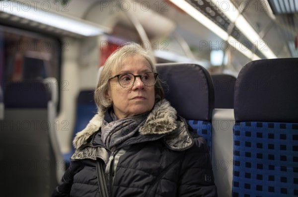 Elderly woman, portrait, thoughtful, glasses, gray hair, coat, scarf, winter clothes, sitting in the S-Bahn, Stuttgart, Baden-Württemberg, Germany
