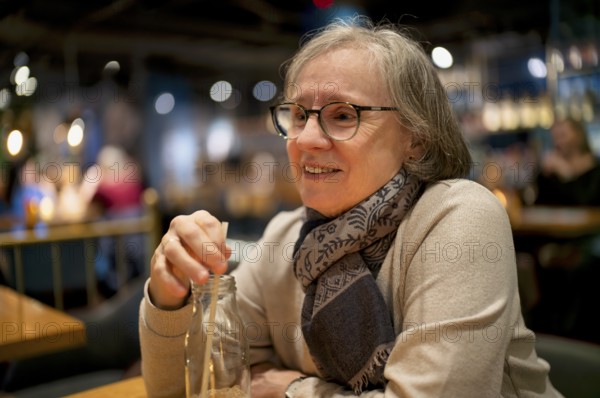 Elderly woman, portrait, glasses, gray hair, scarf, drink, straw, sitting in a bar, restaurant, smiling, Stuttgart, Baden-Württemberg, Germany