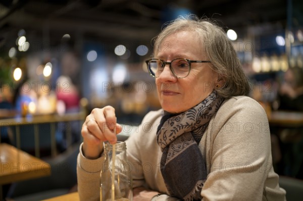 Elderly woman, portrait, glasses, gray hair, scarf, drink, straw, sitting in a bar, restaurant, Stuttgart, Baden-Württemberg, Germany