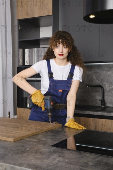 Cheerful young woman assembles the facade of kitchen furniture using a screwdriver