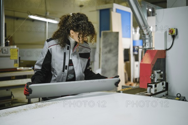 Woman working in a furniture factory inspecting a sheet of material with glued edge tape