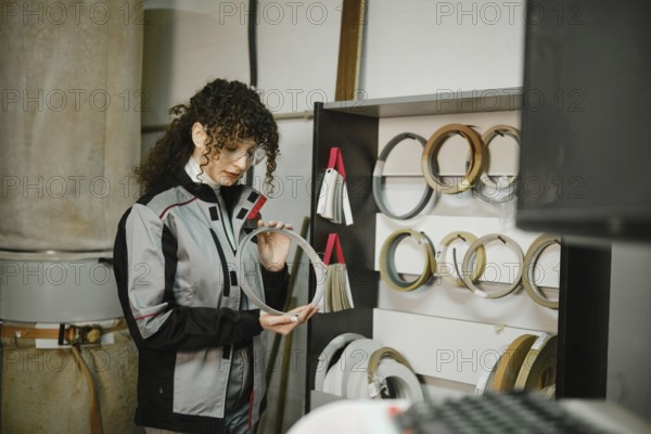 A woman stands in a workshop looking closely at a finishing edge. She is surrounded by various types of edge tapes displayed on a shelf