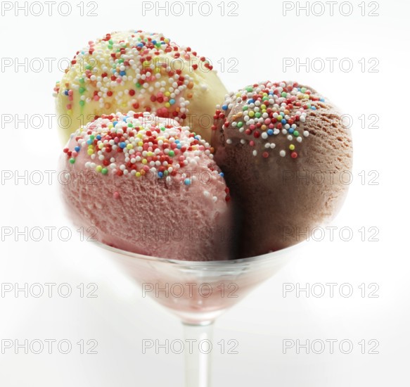 Ice cream sundae with chocolate, strawberry and vanilla, decorated with coloured sprinkles, studio shot against a white background