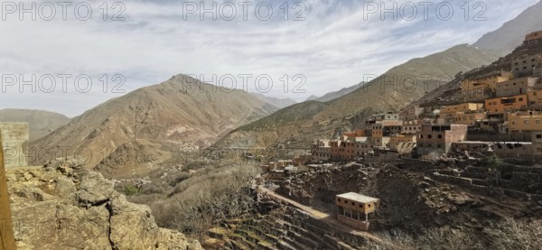A rocky valley with a village in the mountains under cloudy sky, Atlas Mountains, Morocco