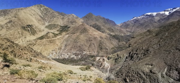 Breathtaking view of a village in a rocky mountain landscape with snow-covered grips under clear sky, Atlas Mountains, Morocco