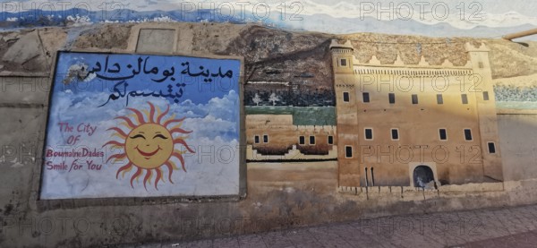 Colourful mural with sun and a depiction of the city in a desert landscape, Morocco