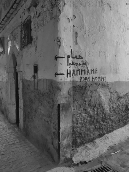Dilapidated wall with graffiti and references to a hammam in a narrow alley, monochrome, old town of Essaouira, Morocco