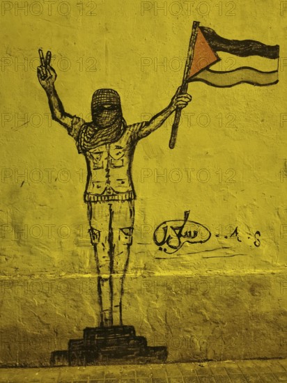 Graffiti of a masked person with Palestine flag showing the victory sign on yellow wall, politically impressive, Casablanca, Morocco