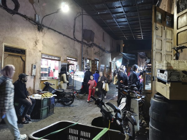 Lively, nocturnal market scene in a narrow alley of the Medina of Marrakech with people and goods, Marrakech, Morocco