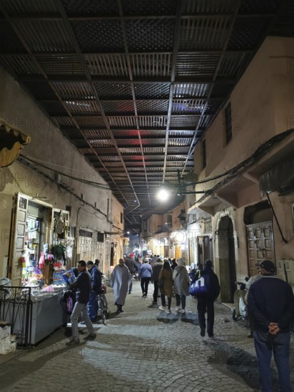 Bustling nocturnal alley in the Medina, with people under a covered path in an oriental market district, Marrakech, Morocco