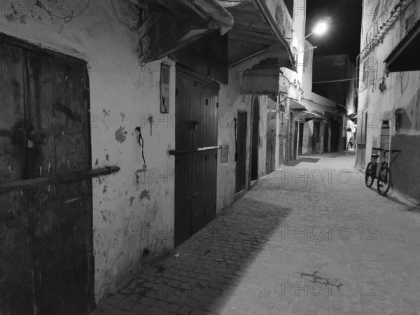 Nocturnal alley with a bicycle and closed doors in an urban setting, monochrome, old town of Essaouira, Morocco