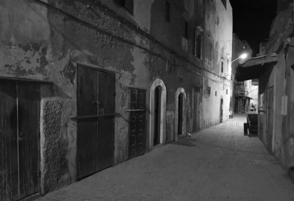 Nocturnal alley with old facades and closed door in a quiet area, monochrome, old town of Essaouira, Morocco