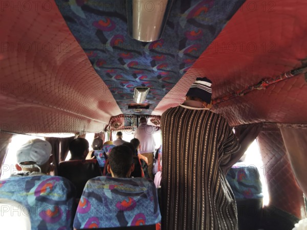 Interior of a bus with colorful seats and a person standing in traditional clothes, Morocco