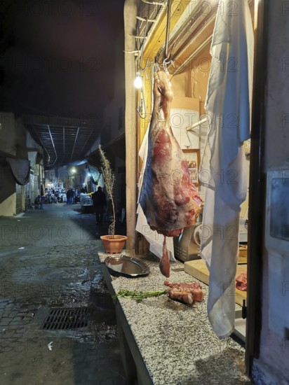 A piece of meat hangs in a shop window on a busy alley of an oriental market, Medina, at dusk, Marrakech, Morocco