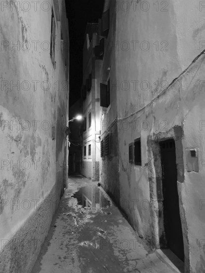 Narrow alley at night with wet floor and atmospheric lighting, monochrome, old town of Essaouira, Morocco