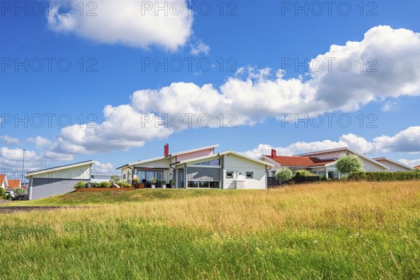 Modern residential houses with white facades and red roofs on grassy hillside under a blue sky with clouds in suburban area, Falköping, Sweden