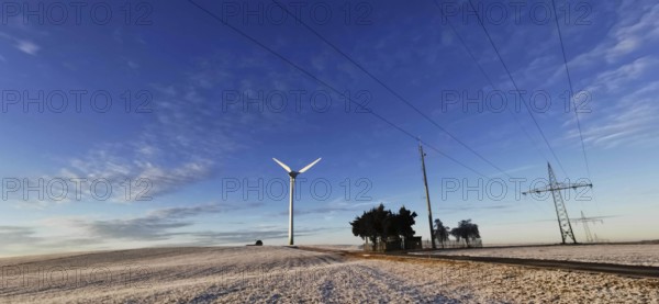 Winter landscape with wind turbine and power lines against a blue sky, Rennsteig, Frankenwald nature park Park