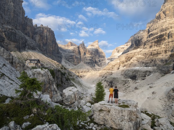 Two hikers in front of impressive mountain peaks of the Brenta Mountains, evening at Refugio Francis Fox Tuckett, Brenta, Parco Naturale Brenta-Adamello, Trentino, Italy