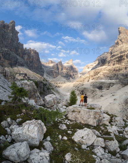 Two hikers in front of impressive mountain peaks of the Brenta Mountains, evening at Refugio Francis Fox Tuckett, Brenta, Parco Naturale Brenta-Adamello, Trentino, Italy