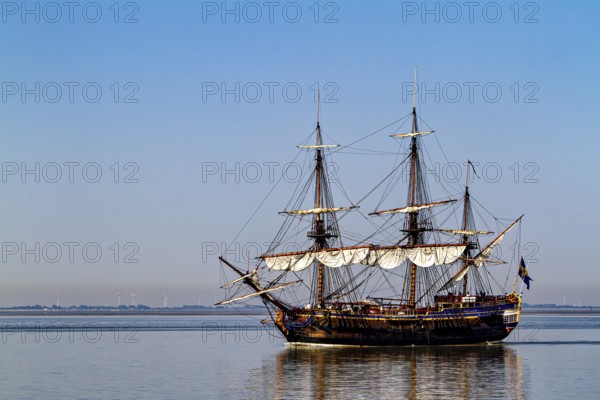 A traditional sailing ship with full sails on calm water under clear blue skies, an old historic sailing ship