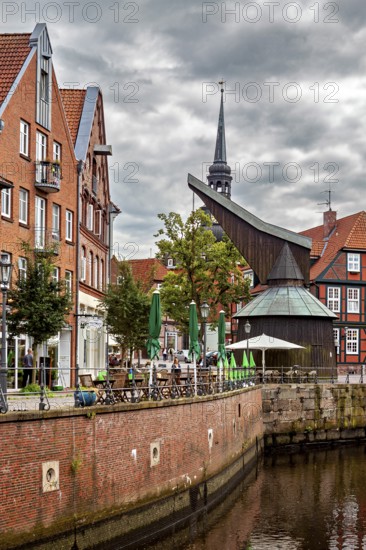 Timber crane and half-timbered houses with a tower on the riverbank under a dramatic sky, The old town of Stade