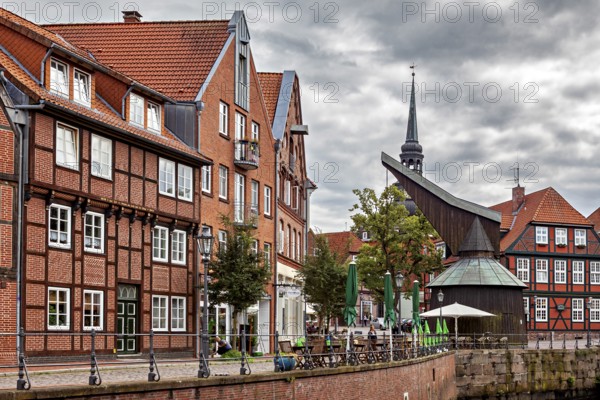 Half-timbered houses and a decorated tower on a riverbank with terraces and cloudy sky, The old town of Stade