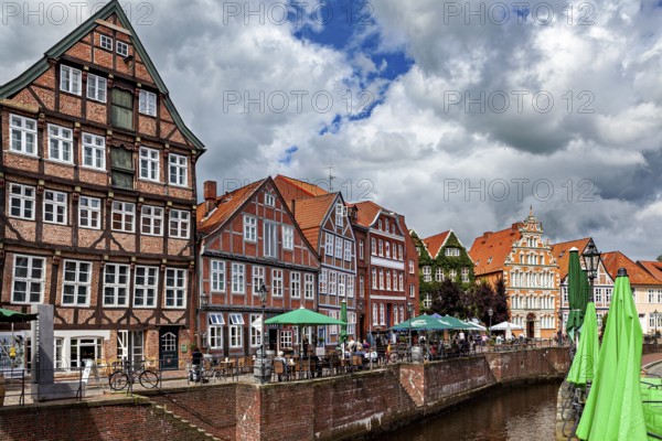 Half-timbered facades and terraces on the river with cyclists and cloudy sky, The old town of Stade