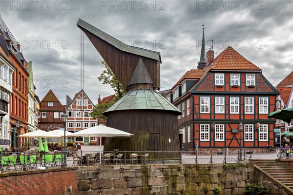 Historic timber crane building and half-timbered houses with terraces under a cloudy sky, The old town of Stade