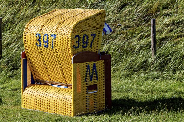 A single yellow beach chair is standing on a green lawn on a sunny summer day, beach chairs on the beach in Cuxhaven