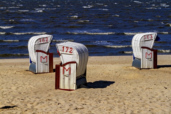 There are three white beach chairs with red numbers on the quiet and sandy beach with waves, beach chairs on the beach in Cuxhaven