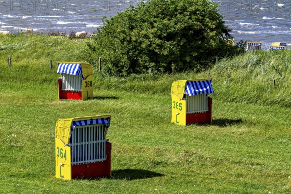 Three colorful beach chairs on a green grassy area with a view of the sea, beach chairs on the beach in Cuxhaven