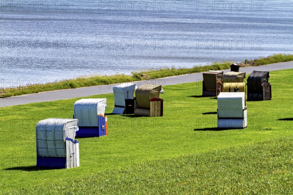 Beach chairs in different colors in a meadow next to a waterside road, beach chairs on the beach in Cuxhaven