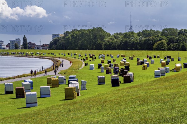 Lots of beach chairs on a green field next to a path with a view of a city in the background, beach chairs on the beach in Cuxhaven