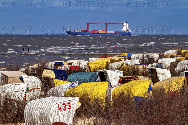 Beach chairs on the beach with a ship on the sea and wind turbines on the horizon, beach chairs on the beach in Cuxhaven