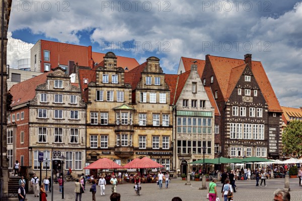 Half-timbered houses in a historic old town. People stroll across a busy market square in cloudy skies, the center of the Hanseatic City of Bremen