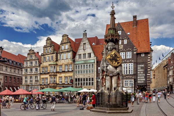 Lively city center with an impressive statue in front of historic buildings under a partly cloudy sky, The Knight Roland on the market square in Bremen