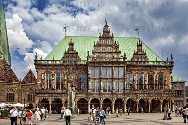 Impressive Renaissance building with green roof and statue, people walking in changeable weather, The Town Hall of Bremen