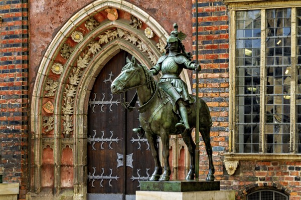 An equestrian statue in front of a Gothic building with richly decorated archway and red bricks, equestrian statue in Bremen
