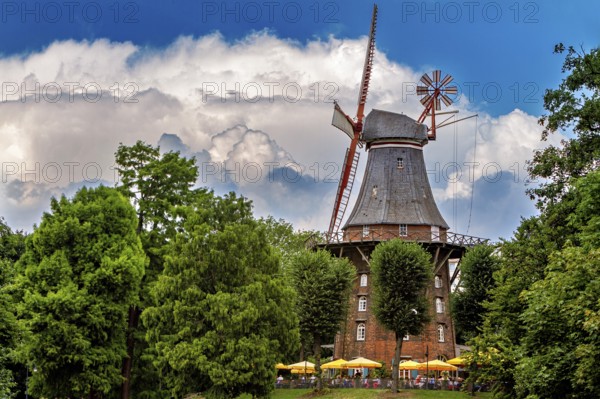 Historic windmill surrounded by trees under blue sky with white clouds and umbrellas, An old historic windmill near Bremen