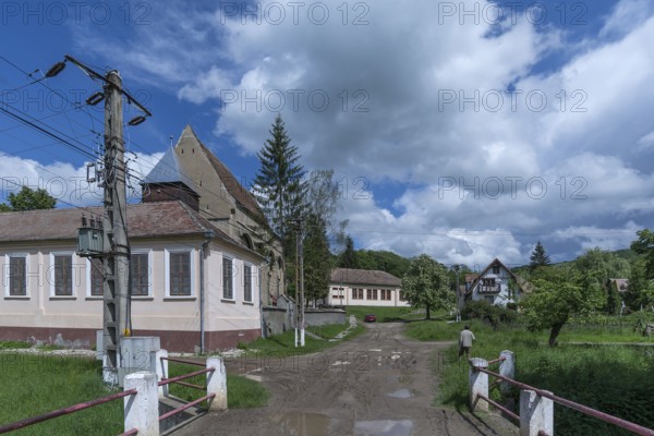 Village street with abandoned 16th century Lutheran fortified church in Tobsdorf, Romanian Dupus, —Transylvania, Romania