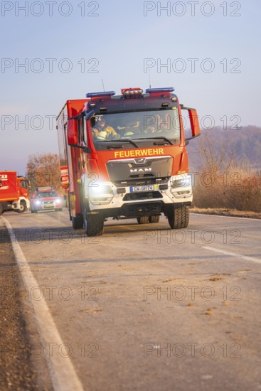 A fire truck on a country road with other emergency vehicles in the background at morning light, fire brigade exercise on the Hermann Hesse Railway, Ostelsheim, Calw district, Germany