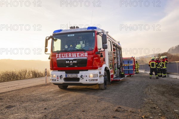 Firefighters stand by a fire truck on the side of the road at sunrise, ready for action, fire brigade exercise on the Hermann Hesse Railway, Ostelsheim, Calw district, Germany