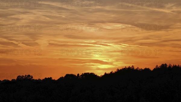 Orange sunset with silhouettes of trees and soft sky, Frankenwald nature park Park