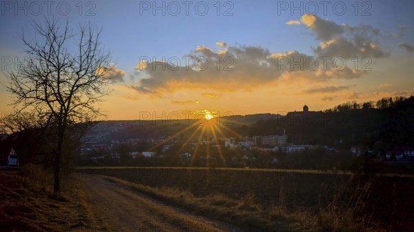 An idyllic sunset over an urban landscape with a path that leads through fields, a view towards Kronach, Frankenwald nature park Park